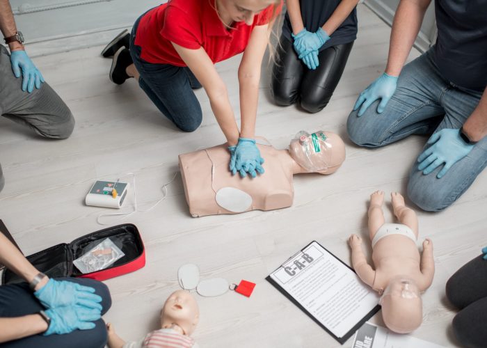 Group of people learning how to make first aid heart compressions with dummies during the training indoors