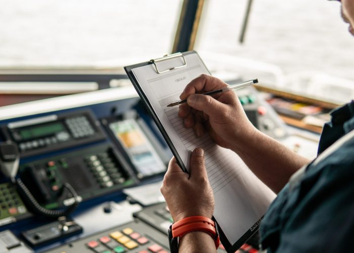 Marine navigational officer or chief mate on navigation watch Marine navigational officer or chief mate on navigation watch on ship or vessel. He fills up checklist. Ship routine paperwork