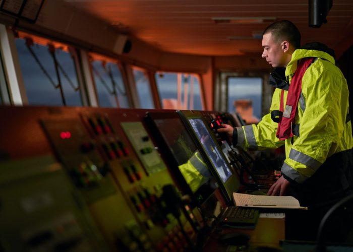 Navigator. pilot, captain as pat of ship crew performing daily duties with VHF radio, binoculars on board of modern ship with high quality navigation equipment on the bridge on sunrise. Navigator. pilot, captain as pat of ship crew performing daily duties with VHF radio, binoculars, logbook, standing nearby to ECDIS and radar station on board of modern ship with high quality navigation equipment on the bridge. Great design for navigation, safety of shipping, cargo carriage puproses.